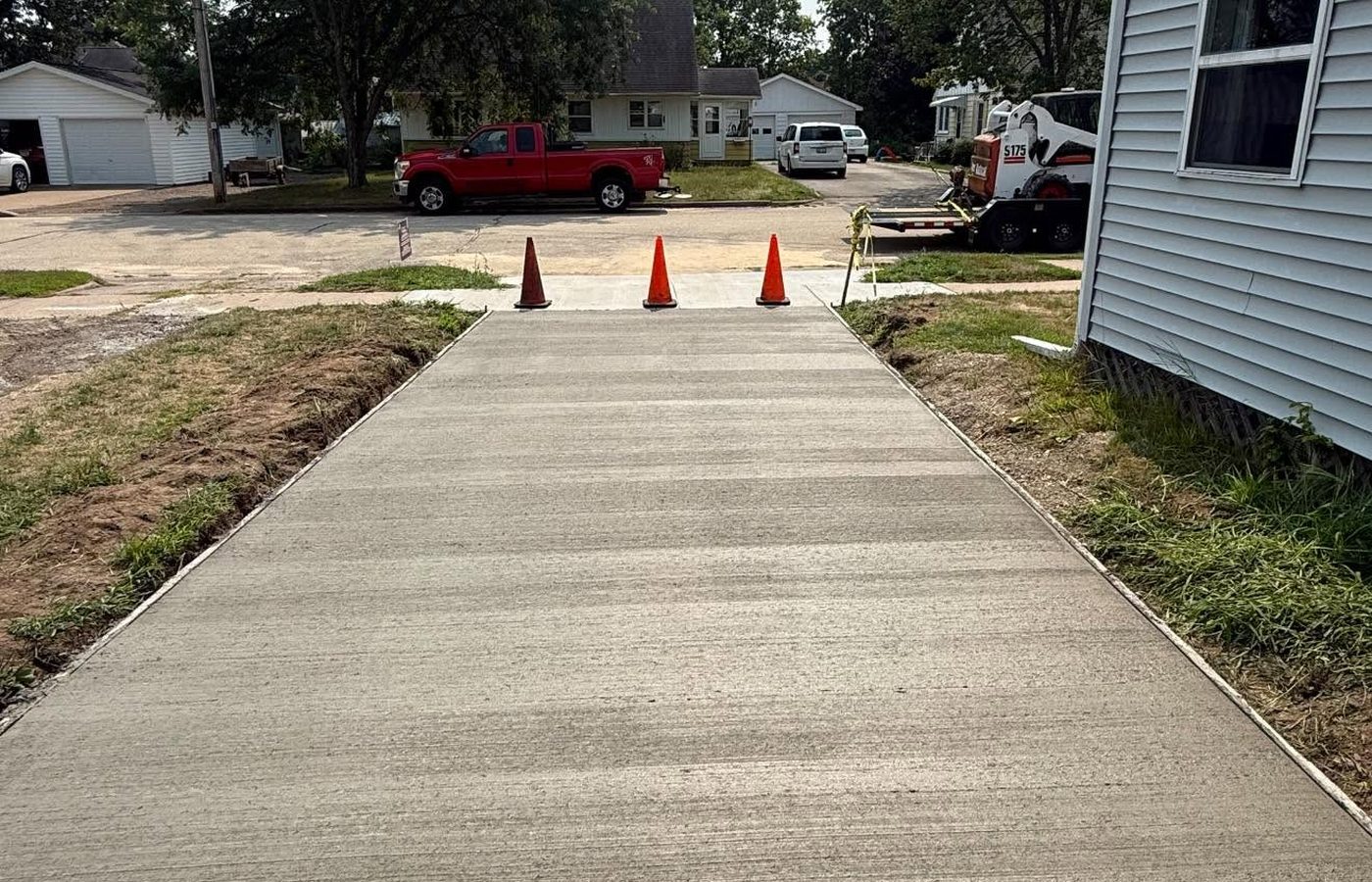 A fresh concrete walk poured beside a house, cones at the street end