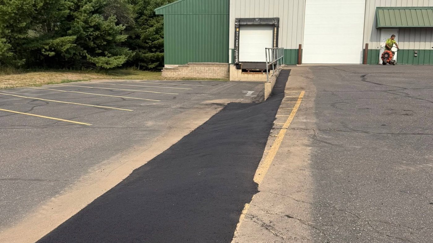 A fresh asphalt drive lane running up to a loading dock door at an industrial building, new yellow lines beside it