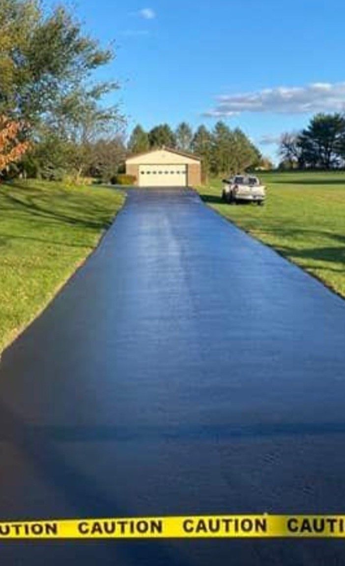 A freshly sealcoated driveway still glistening, caution tape across the entrance