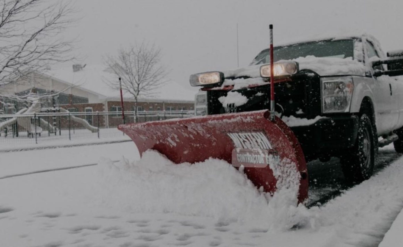 A pickup with a red plow pushing a windrow of snow across a lot