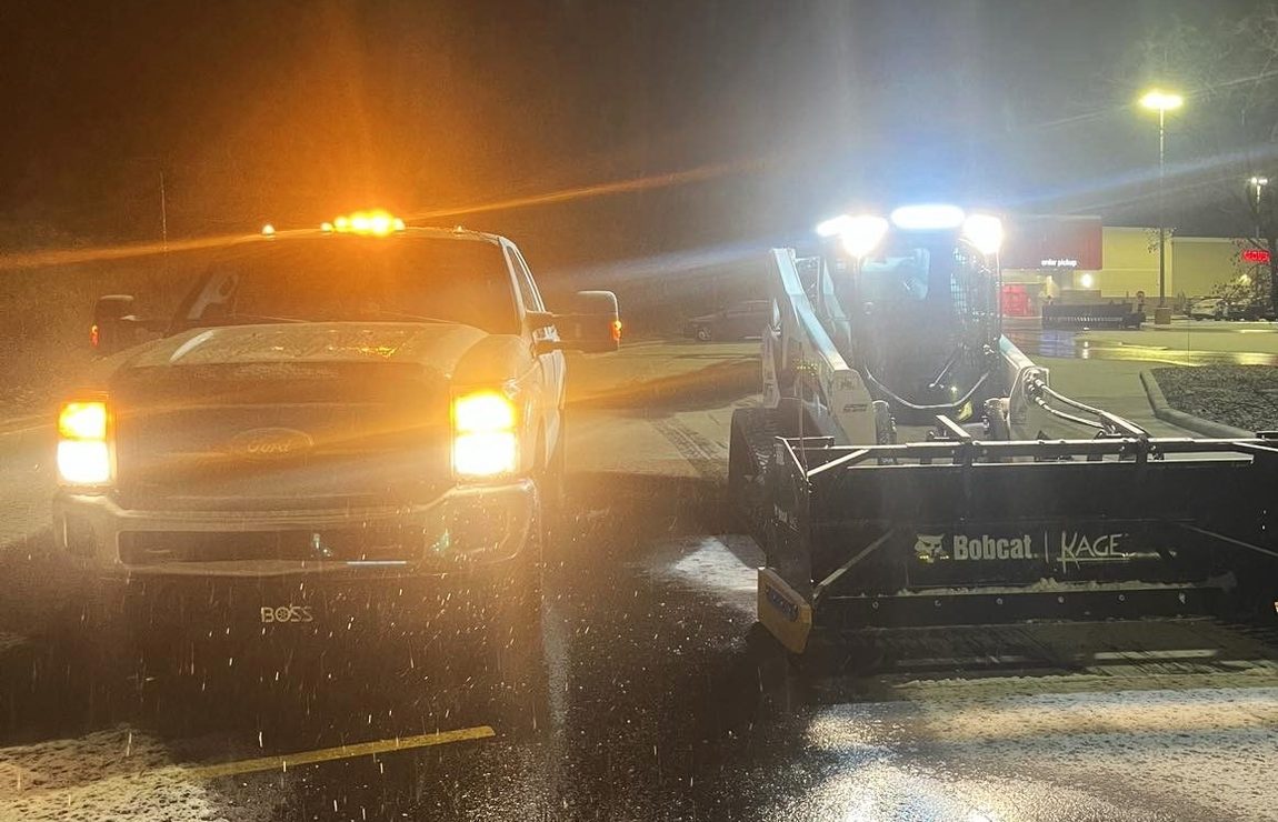 The plow truck and a Bobcat with a snow pusher working a lot at night